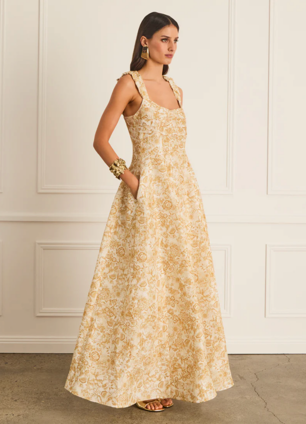 Woman wearing a long floral dress against a white wall