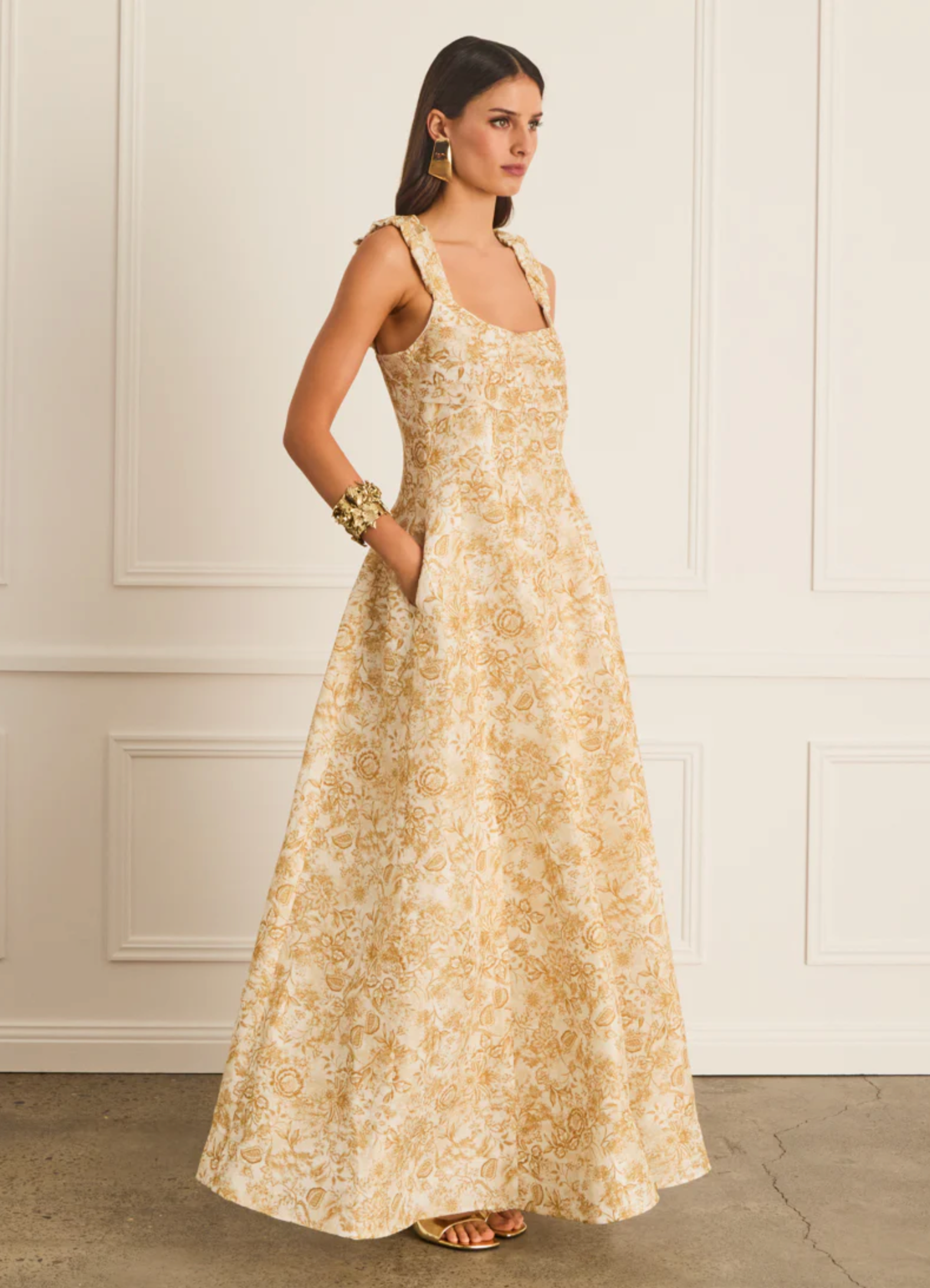 Woman wearing a long floral dress against a white wall