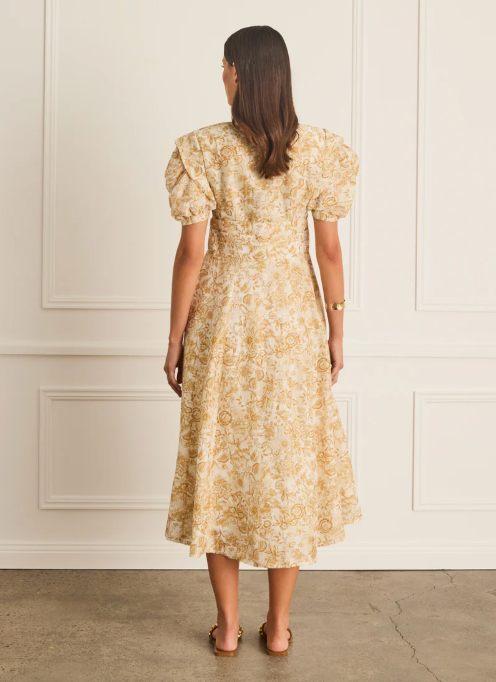 Woman wearing a floral dress against a white paneled wall.