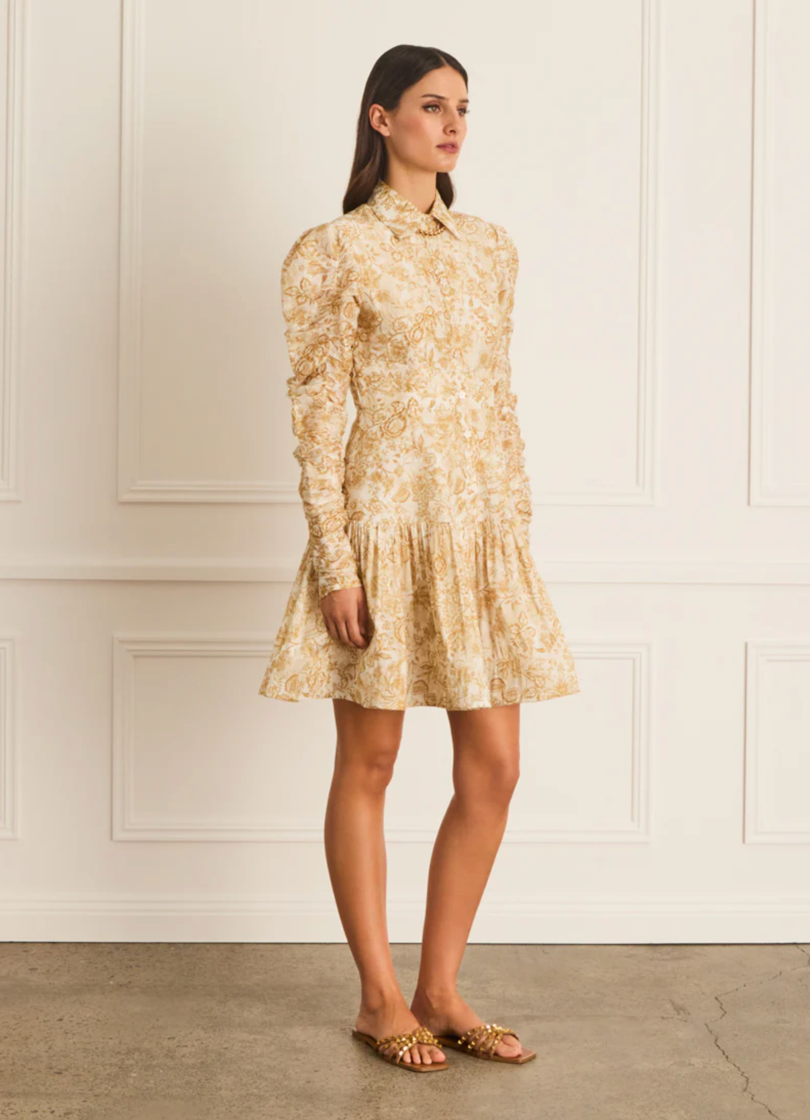 Woman wearing a floral dress against a white paneled wall.