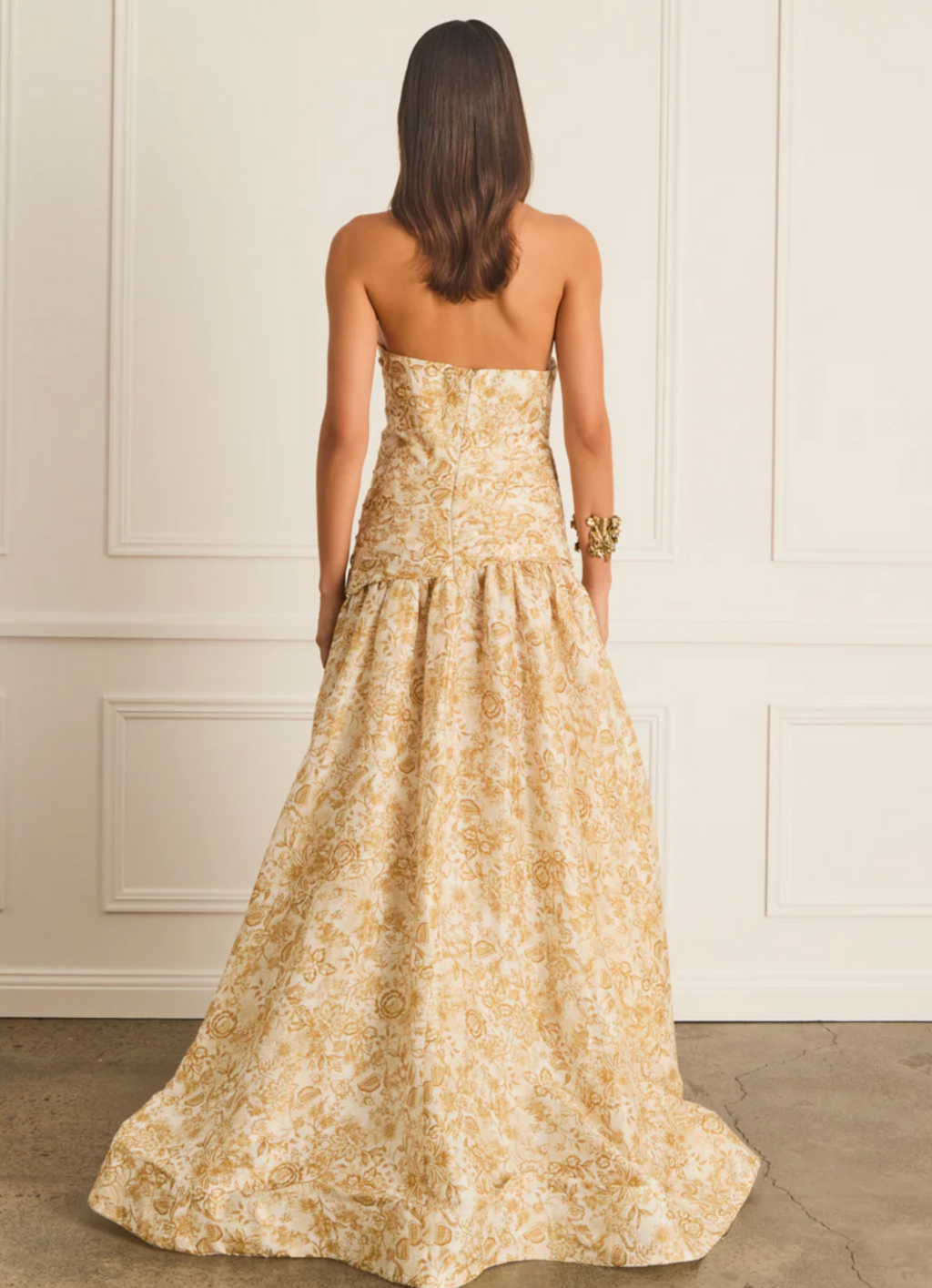 Woman wearing a strapless floral dress against a white wall.
