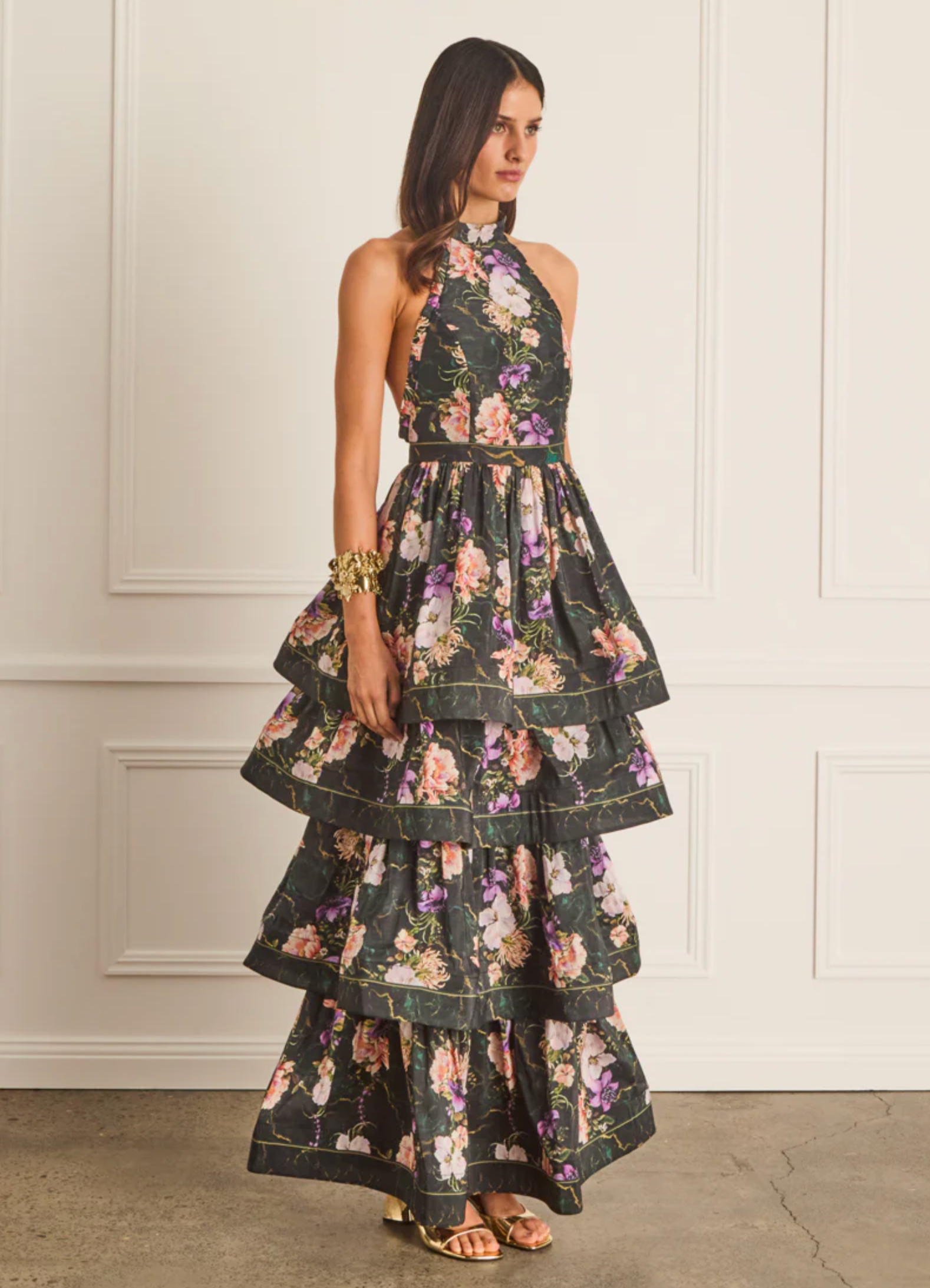 Woman wearing a floral tiered dress against a white wall.