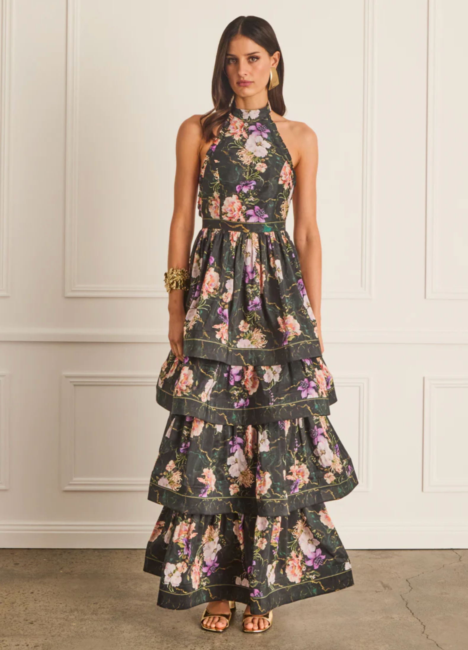 Woman wearing a floral tiered dress against a white paneled wall.