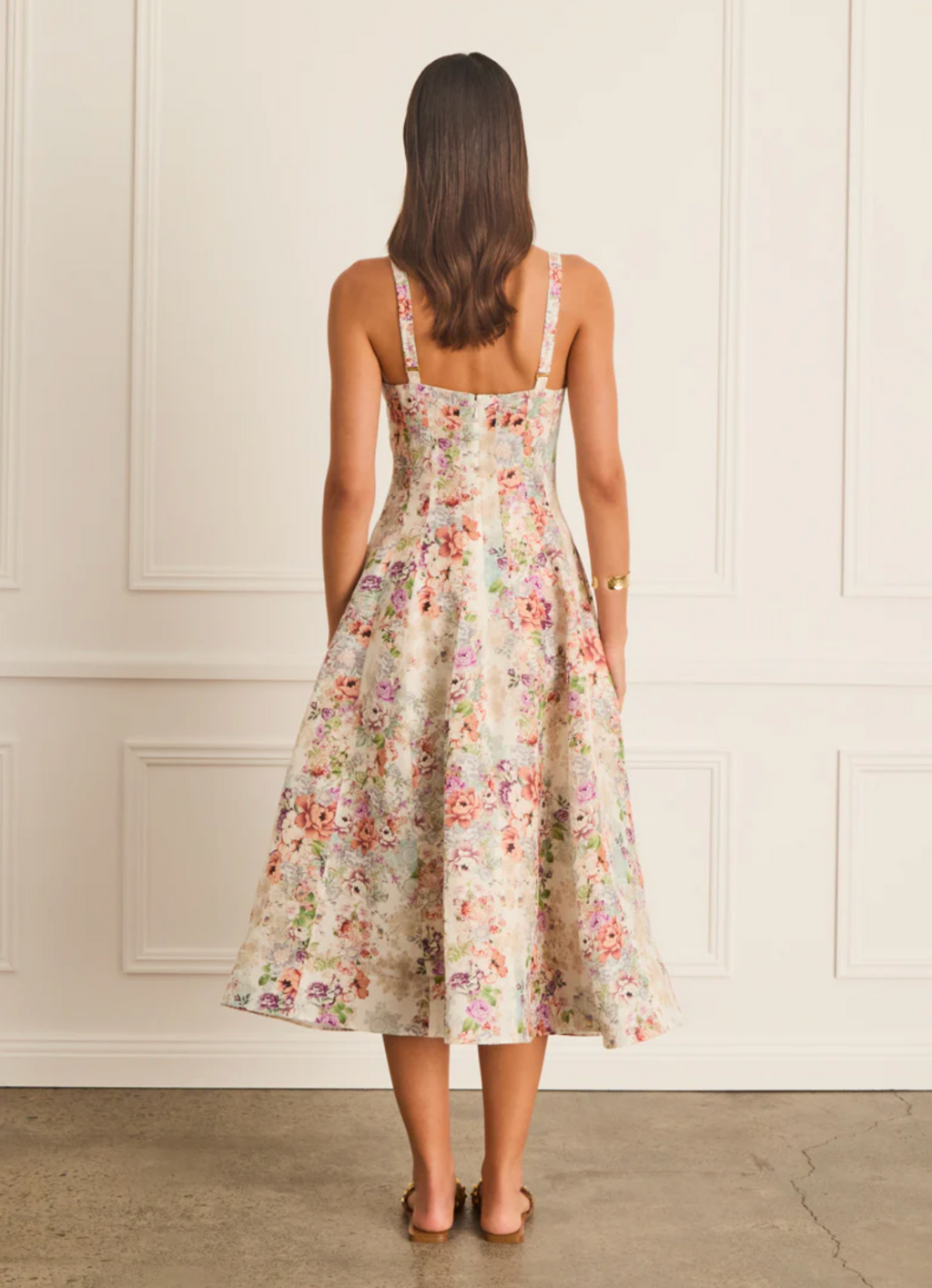 Woman wearing a floral dress standing against a white paneled wall.