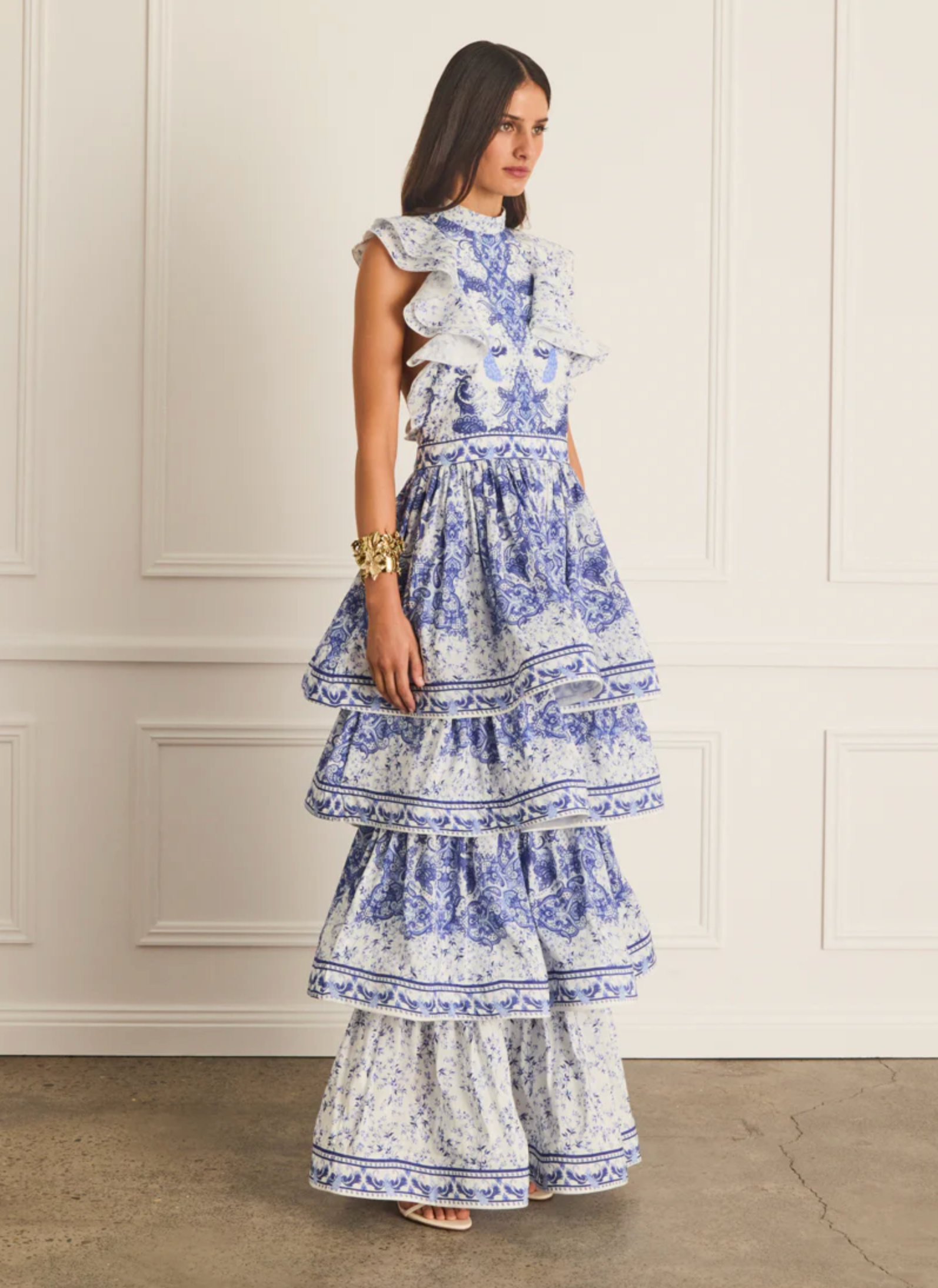 Woman wearing a blue and white floral dress against a white wall.
