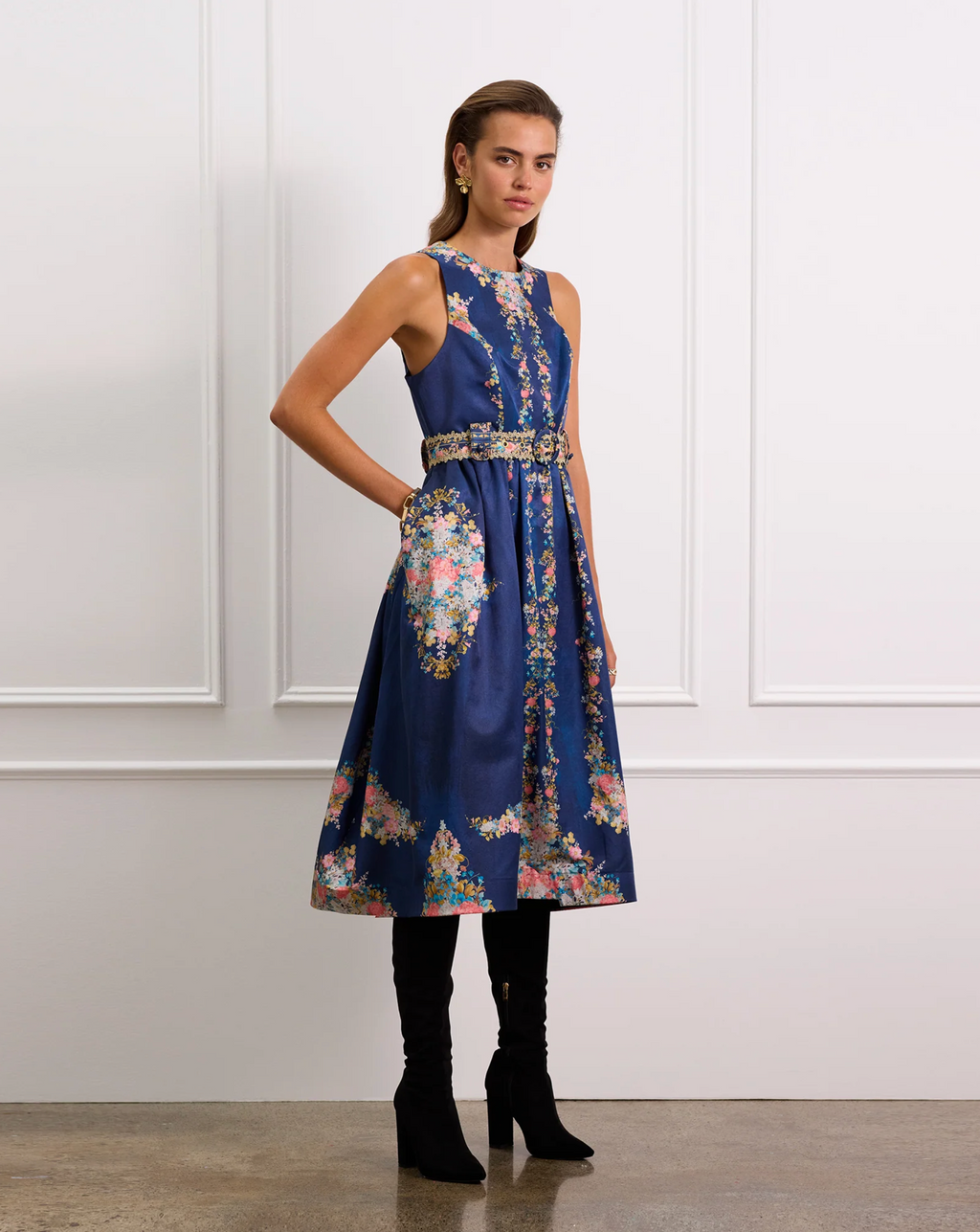Woman wearing a blue floral dress with a belt in a room with white paneled walls.
